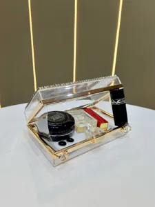 Clear acrylic evening clutch bag detail shot with gold metal frame and rhinestone top trim.