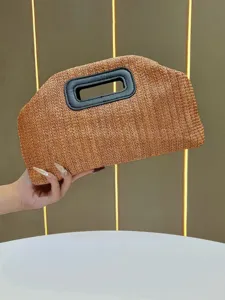 Straw woven clutch bag detail view, natural texture and black leather handle design.