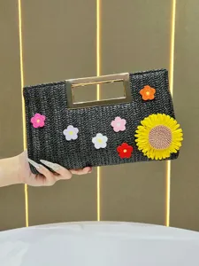 Detailed view of black woven straw clutch bag with golden metal handle and colorful crochet flowers.