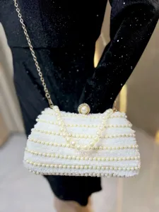 Detailed shot of white beaded evening clutch bag with pearl handle and gold chain strap.