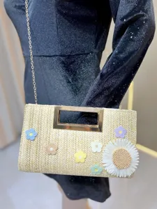 Close-up of stylish straw clutch featuring delicate crochet floral design and gold metal handle.