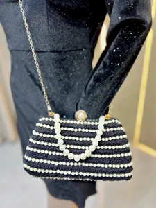 Detailed shot of black beaded evening clutch with white pearl stripes and gold chain.