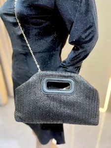 Detailed view of a stylish black woven straw handbag with gold chain strap and structured handle.