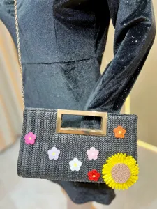 Chic black straw woven crossbody bag with metal handle and colorful crochet flowers detail.