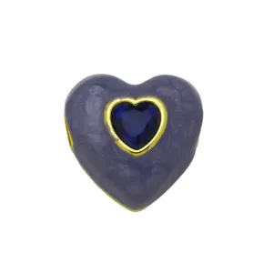 Dettaglio in primo piano di un ciondolo cuore smaltato viola con zircone blu brillante.