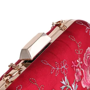 Close-up detail of red embroidered evening clutch bag, showing gold metal clasp and floral stitching.