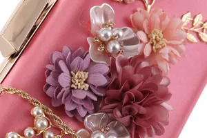 Close-up detail of women's pink satin evening clutch bag with floral pearl and gold chain.