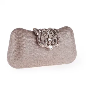 Detail shot of elegant rhinestone crown clasp evening clutch bag, sparkly gold hard shell surface.