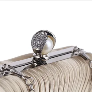 Detail shot of pleated evening clutch bag featuring rhinestone pearl clasp and chain strap.