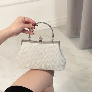 Close-up of white beaded evening bag with metallic handle and clasp for elegant banquet wear.