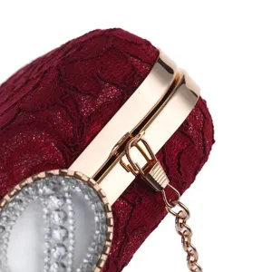 Detalle de bolso de mano de encaje rojo vino, elegante marco de metal dorado y cierre de brillantes.