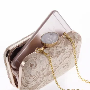 Bolso de mano de encaje beige con marco de metal, cierre de estrás y cadena dorada.