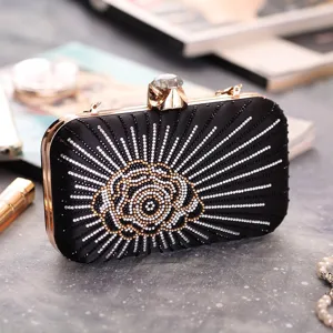 Black rhinestone evening clutch bag detail showing sparkling crystal clasp and gold metal frame.
