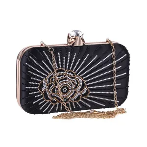 Detail view of black satin evening clutch featuring sparkling rhinestone rose and gold chain.