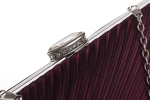 Close up detail of wine red pleated evening clutch bag with rhinestone clasp and metal chain.