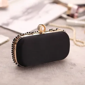 Black evening clutch bag detail showing gold metal frame with pearl rhinestone clasp.