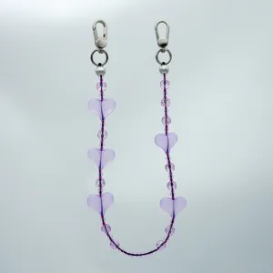 Detailansicht einer lila Perlen-Handykette mit durchsichtigen Herz-Anhängern und Metallverschlüssen.