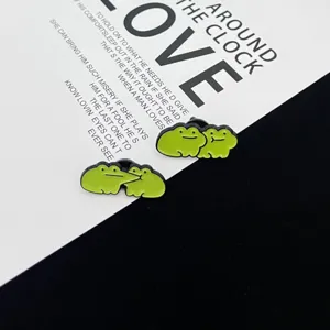 Close-up detail of cute green frog enamel couple brooches, stylish cartoon pin accessories.