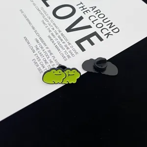 Close-up detail of cute green frog couple enamel pin, showing front design and back clasp.