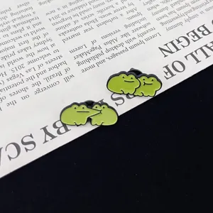 Close-up of cute green frog couple enamel pins, lovely cartoon brooch for clothes decor.
