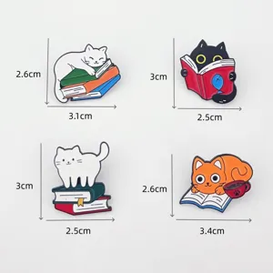 Close-up detail shot of adorable cat enamel brooches showing dimensions and book-reading style.