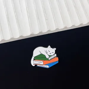 Detail shot of a creative cat enamel pin featuring a cute white cat sleeping on a colorful stack of books.