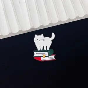 Detailed close-up shot of the cute cat enamel pin standing on books, perfect metal badge.