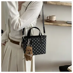 Nahaufnahme der schwarzen Pünktchen Eimer Handtasche mit süßem Hundemotiv Anhänger.