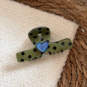 Detailaufnahme einer grünen Haarklammer mit schwarzen Punkten und blauem Herz auf weichem Stoff.