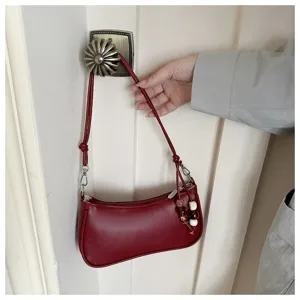 Red leather baguette shoulder bag detail showing smooth texture and elegant beaded charm accessory.