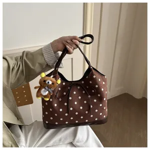 Vista dettagliata della borsa a tracolla marrone a pois con elegante fiocco e ciondolo orsetto.