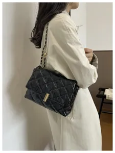 Scatto di dettaglio di una borsa a tracolla matelassè in pelle verniciata nera con catena.