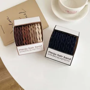 Vista detallada de coleteros elásticos para el cabello en cajas marrones y negras con atrezzo.