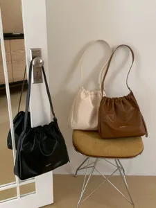 Detail view of casual pleated cloud shoulder bags in black, beige and brown interior scene.