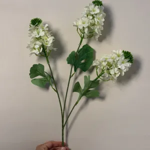 Dettaglio di ramo di fiore di delphinium bianco artificiale con petali e foglie verdi.