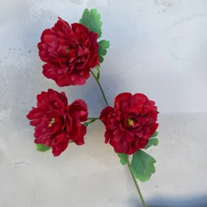 Nahaufnahme Detail von künstlichem roten Blumenast mit drei Blüten und grünen Blättern für Deko.