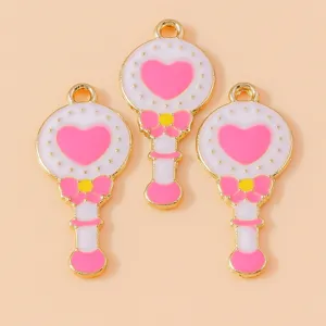Close-up detail shot of cute magical wand enamel charms with pink heart and gold trim.