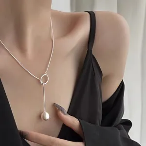 Detalle en primer plano de un collar de plata con colgante de bola cepillada en el cuello.