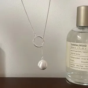 Primer plano de un collar de plata minimalista con colgante de bola cepillada y anillo.