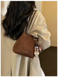 Brown suede bucket bag detail showcasing elegant metal rings and cute flower charm accessory.