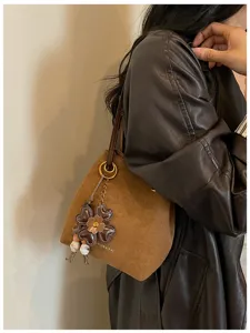 Vintage brown suede bucket bag with stylish flower charm and shoulder strap for women.