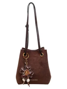 Brown suede bucket bag for women, stylish shoulder crossbody bag with cute flower charm accessory.