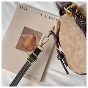 Brown suede crossbody bag detail showing metallic hardware, adjustable leather strap and retro style.