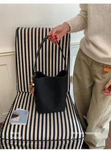 Détail de sac seau tressé noir chic, sac porté épaule élégant pour le travail et l'été.
