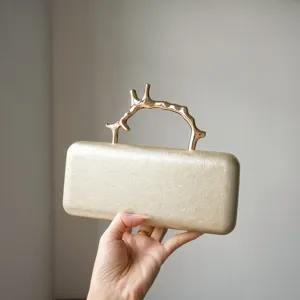 Gold evening clutch detail showing unique metal branch handle and premium leather texture.