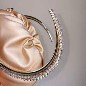 Detailed view of luxury champagne satin pleated evening clutch bag with sparkling rhinestone handle.
