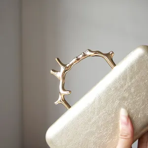 Detailed view of the luxury gold evening clutch featuring a unique metallic branch handle.