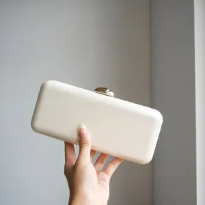 White evening clutch bag detail showing premium leather texture and elegant gold clasp design.