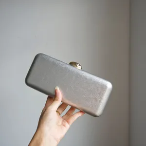 Silver metallic clutch bag detail view, premium leather texture with elegant gold clasp design.