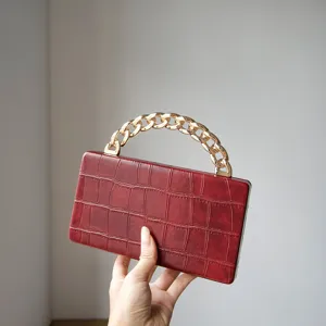 Detailed view of the red crocodile texture hard clutch bag with a chunky gold chain handle.